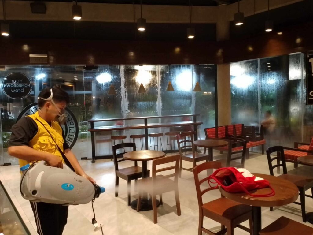 **Alt text:** Technologist Pest Control technician performing ULV misting disinfection inside a restaurant, wearing safety gear and using a fogging machine to sanitize the area.